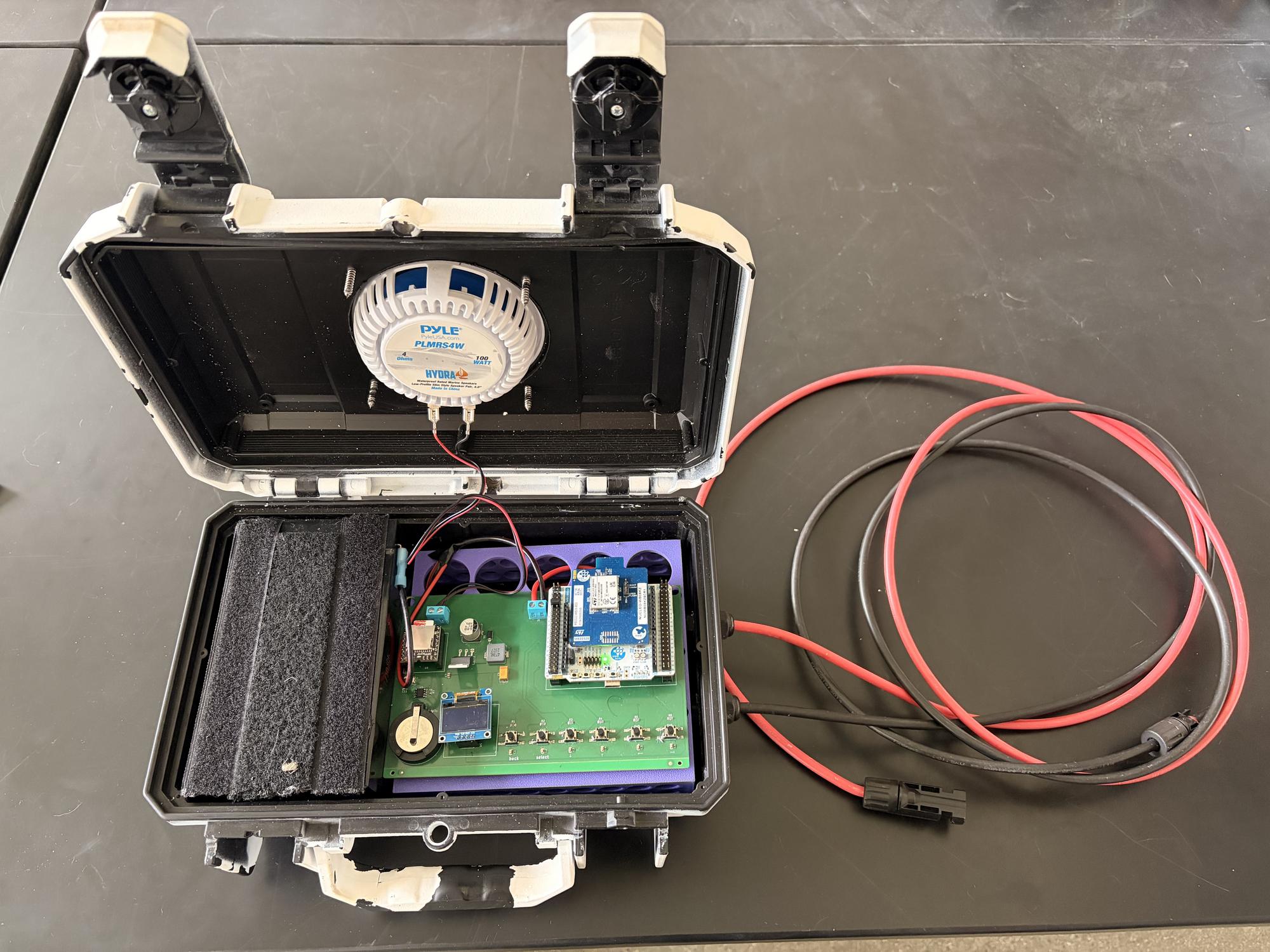 Interior of an Ambiance playback speaker. Visible components are the lithium iron phosphate battery (left), custom printed circuit board (right), and 4" inch Pyle speaker top. Not pictured is the solar panel which would attach the the red and black solar extension cables outside the housing. There is an MPPT solar controller housed underneath the purple bracket that the printed circuit board mounts to.